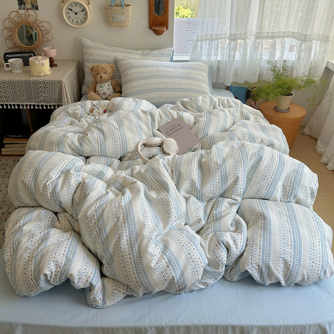 Light blue floral stripe duvet cover set styled with lace curtains, teddy bear, and soft bedding layers.