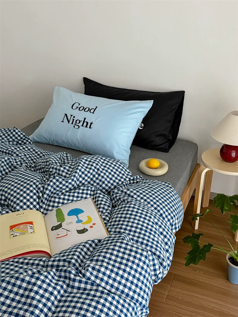 Bed with checkered blue and white duvet, black pillow, and 'Good Night' pillow.