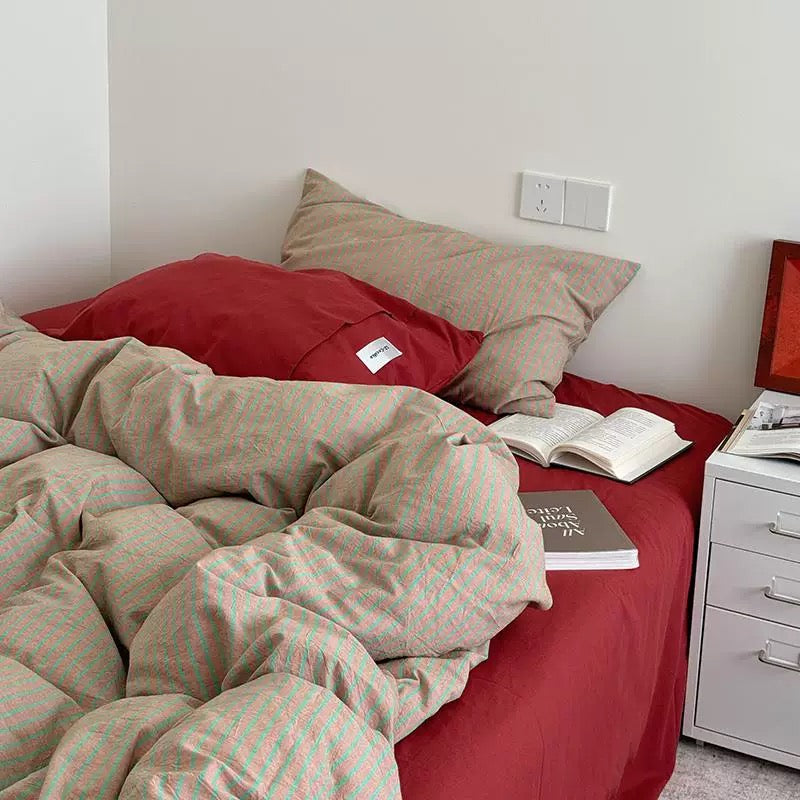 Bed with red sheets and beige pillows, next to a nightstand with a book and magazine.