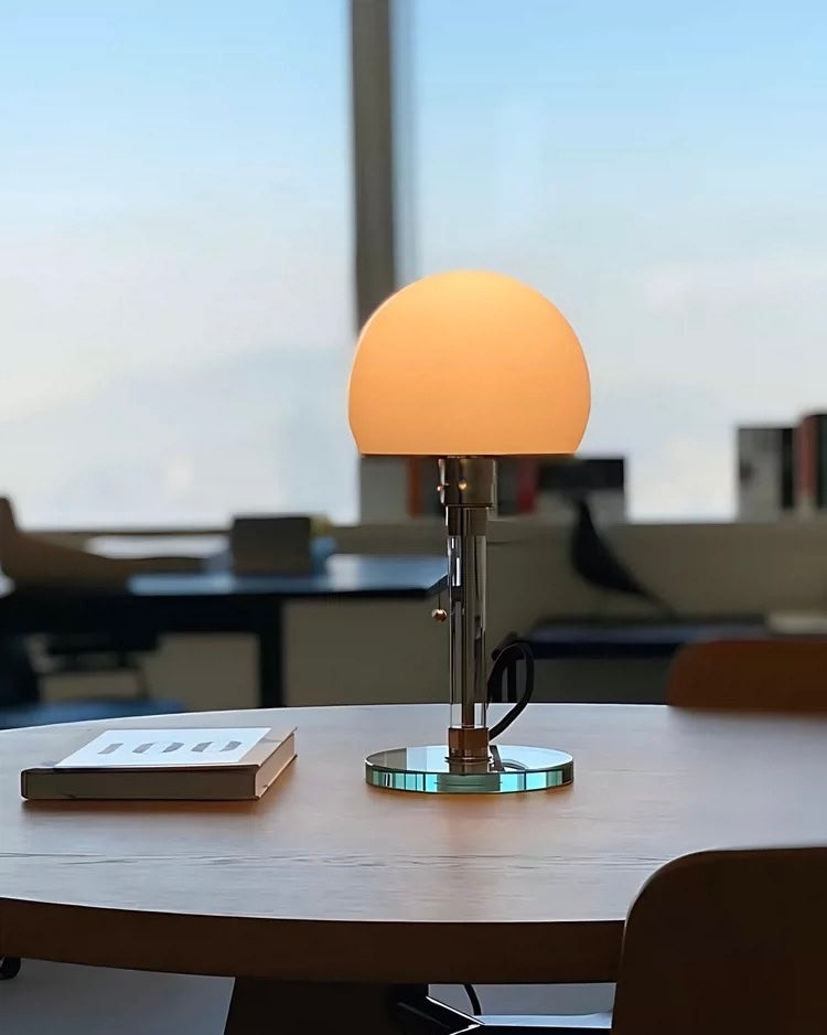 Chrome mushroom table lamp with warm dome shade styled on white bedside table with books.