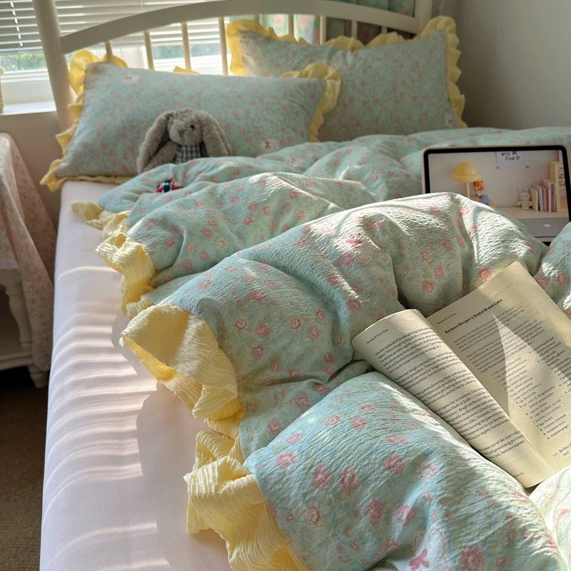 Two floral ruffle pillowcases arranged on a bed beside an open book and plush bunny
