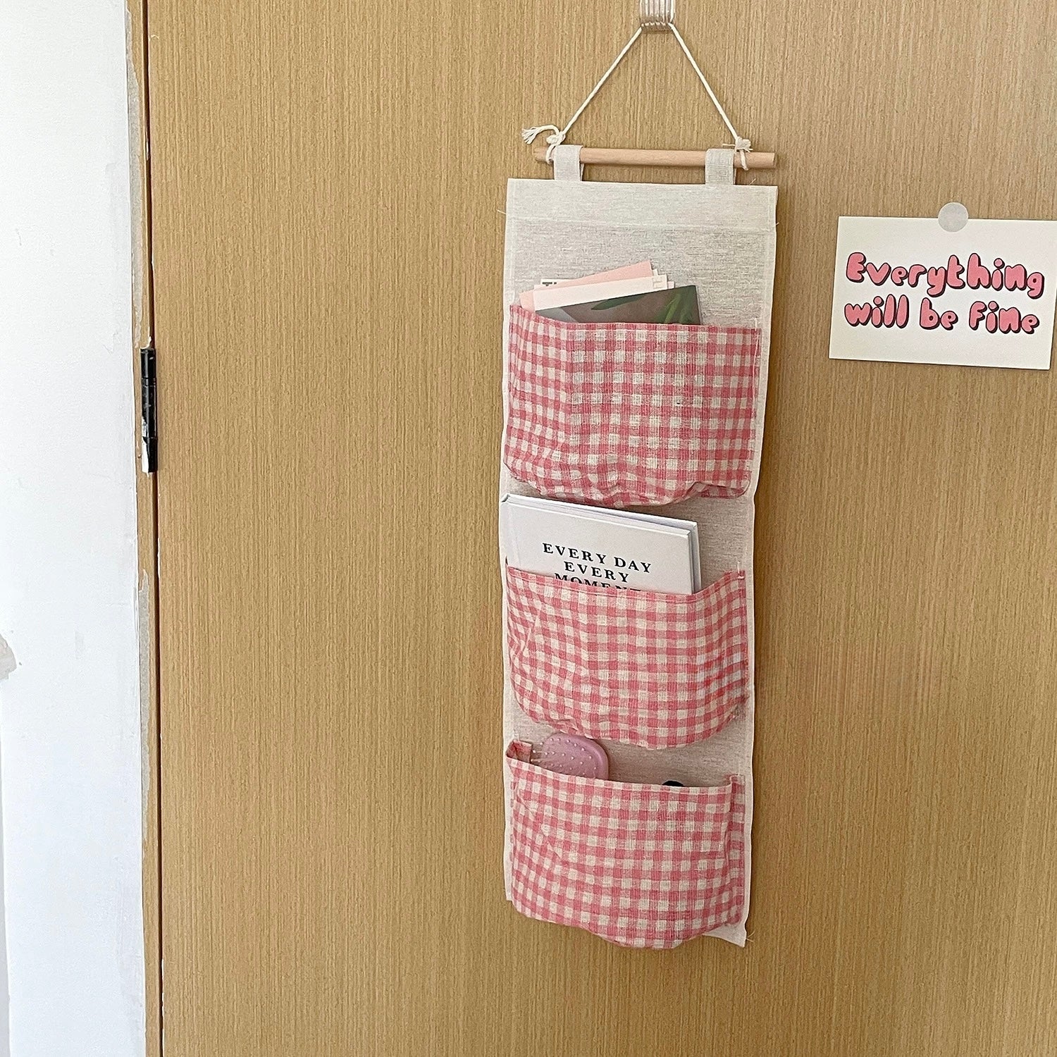 Wall-mounted organizer with pink gingham design hanging on a wooden door.