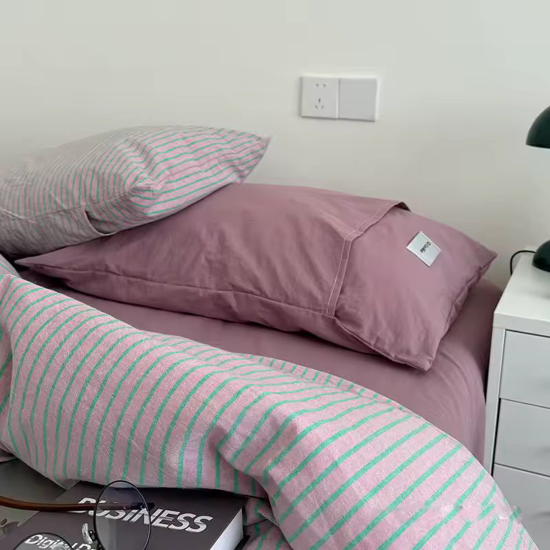 Pink and green striped bedding on a bed with a nightstand in the background.