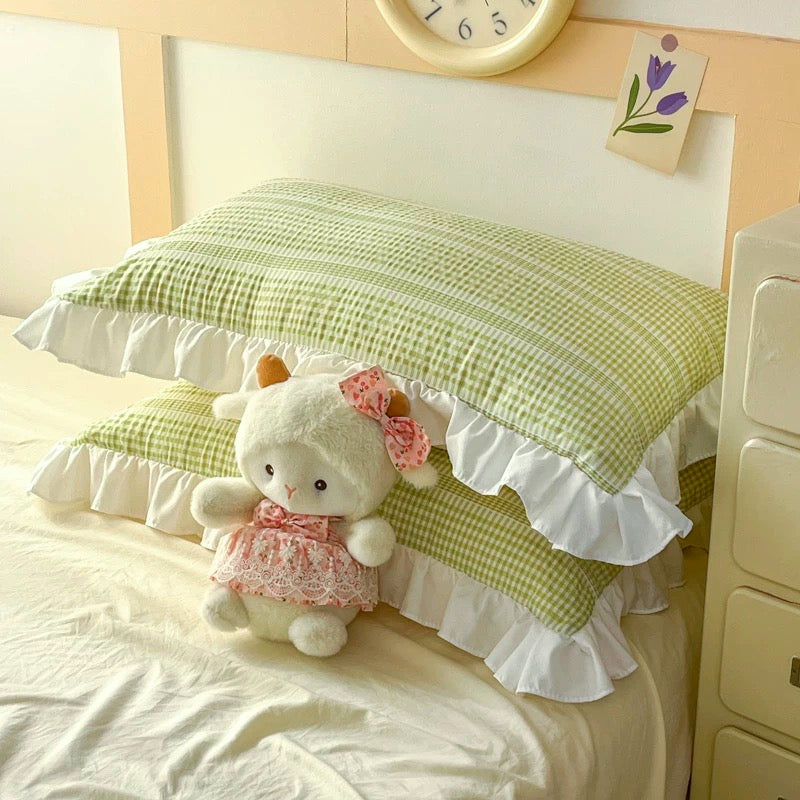 Green checkered pillow with ruffles and a plush toy on a bed.
