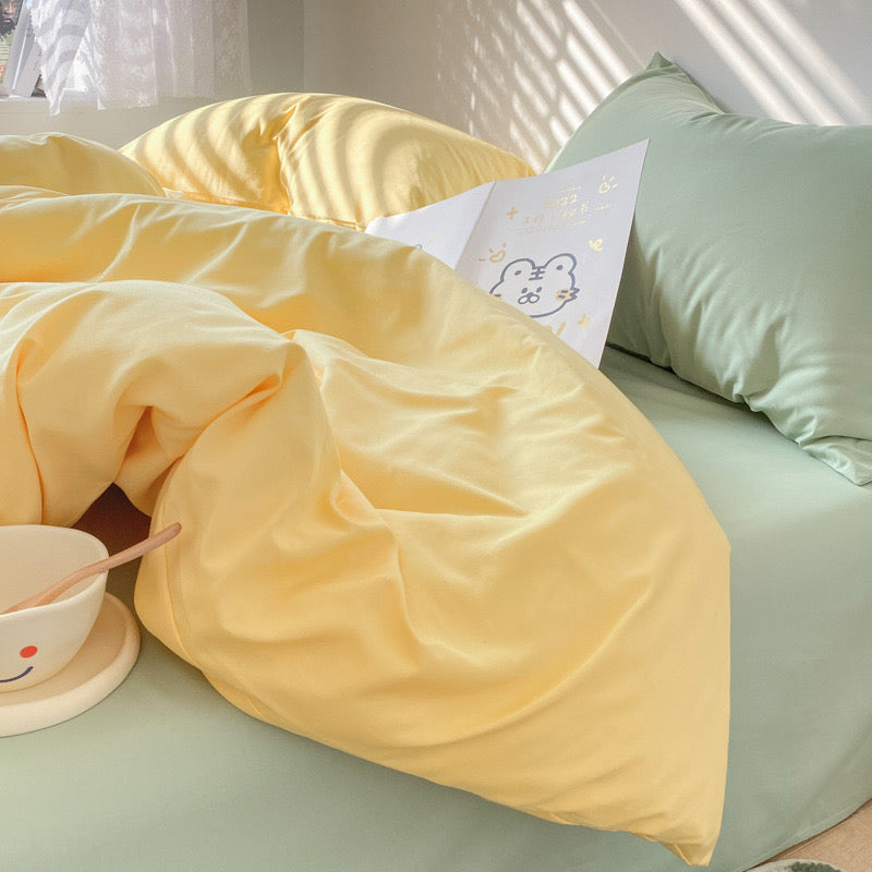 Yellow blanket on a bed with a green pillow and a small white card.