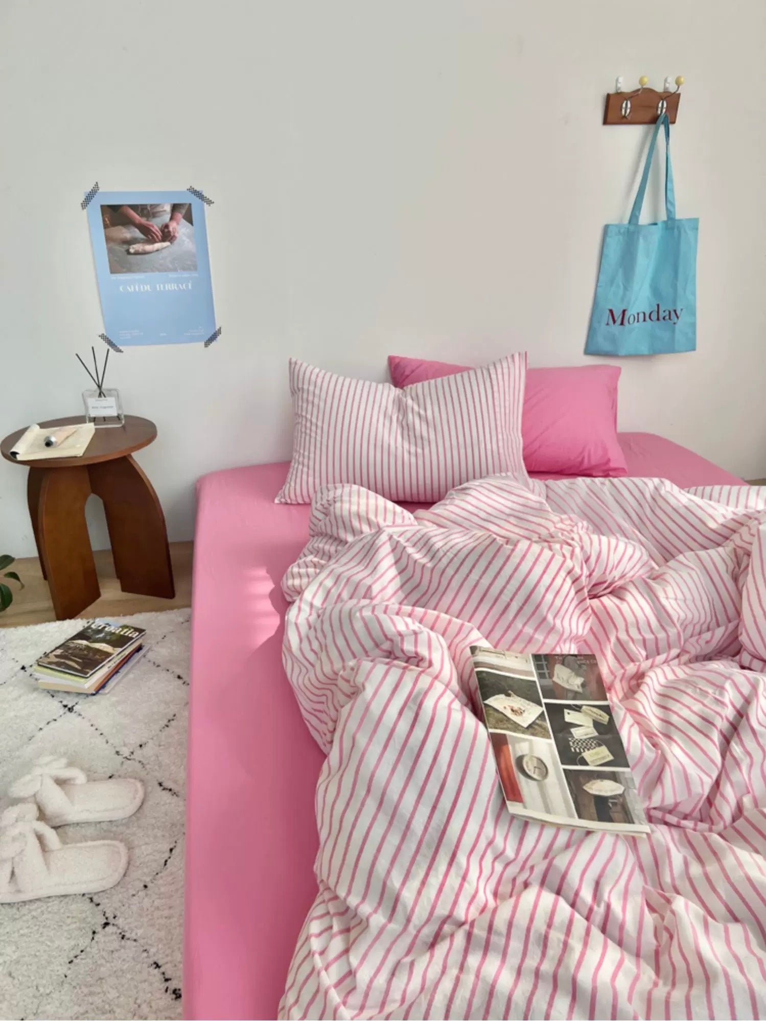 Pink bed with striped bedding in a room with a small table and wall decorations.
