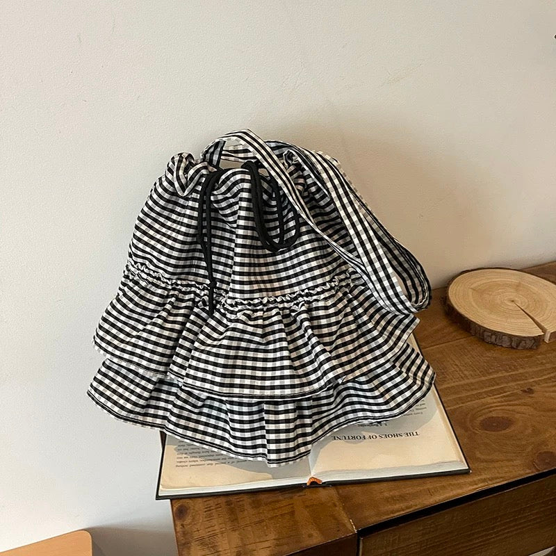 Black and white checkered bag on a wooden surface with a book underneath