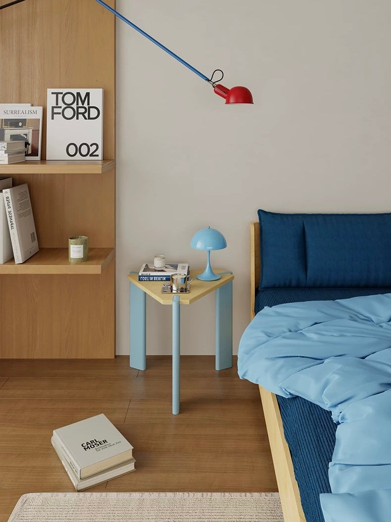 Light blue bedside table with a triangular wood top holding a blue lamp beside a bed with blue bedding.