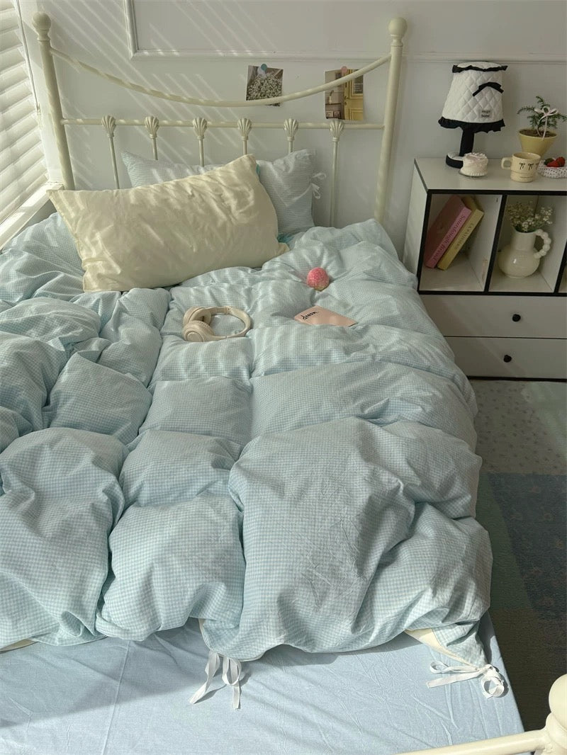 Light blue textured comforter on a bed with pillows and a nightstand in the background.