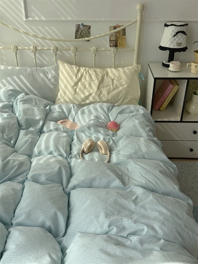Light blue textured comforter on a bed with pillows and a nightstand in the background.