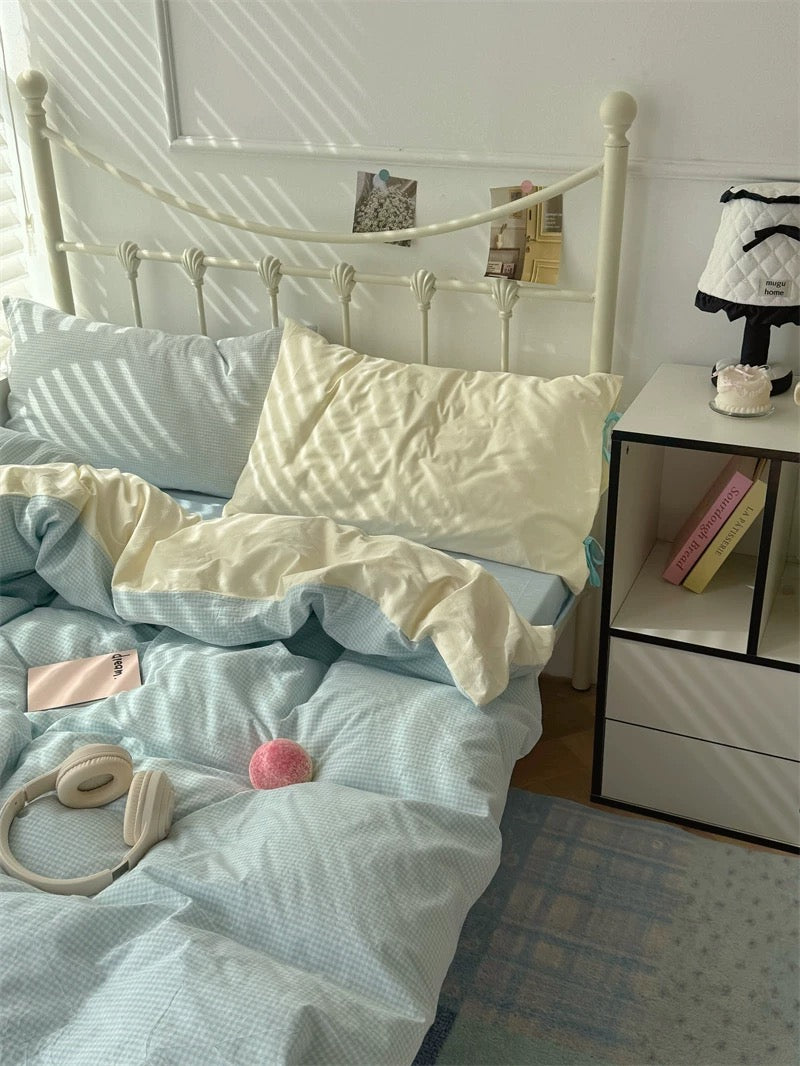 Bedroom with a white metal bed frame, light blue bedding, and a nightstand with books and a lamp.