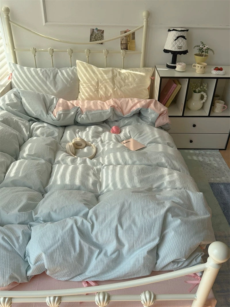 Bed with light blue comforter and pink pillows in a bedroom setting.