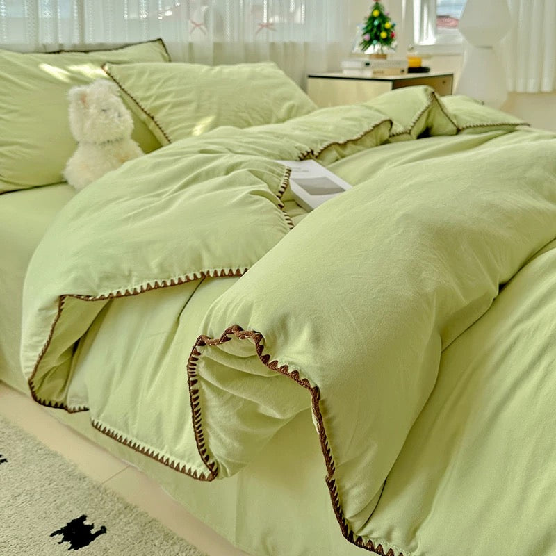 Light green bedding set on a bed with a teddy bear in a bedroom setting.