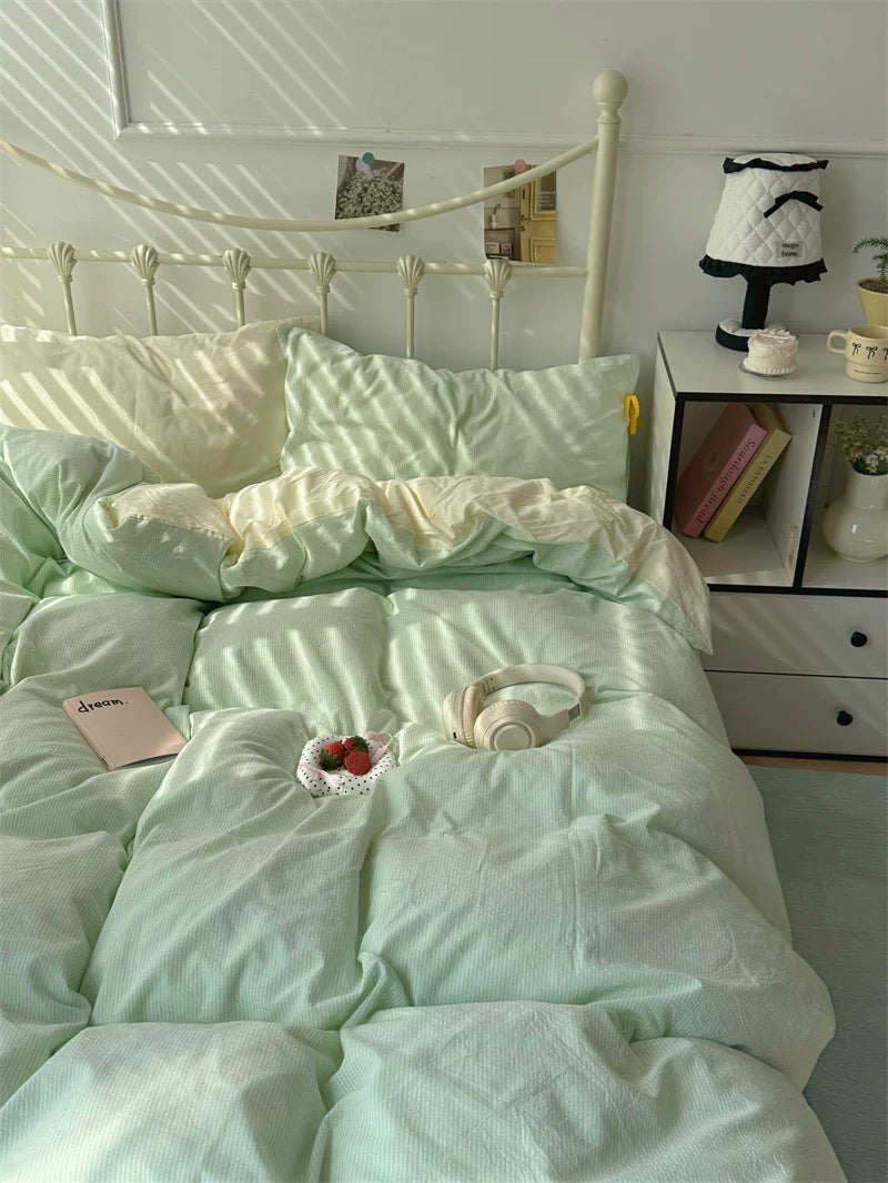 Light green bedding set on a bed with a nightstand and decor items in the background.
