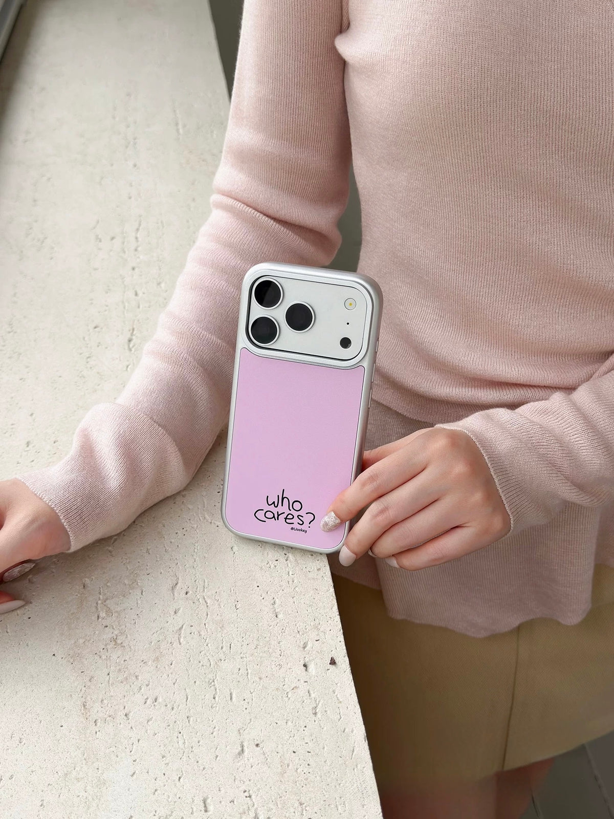Light pink phone case held upright, with a silver colored border and small black lettering on the back.
