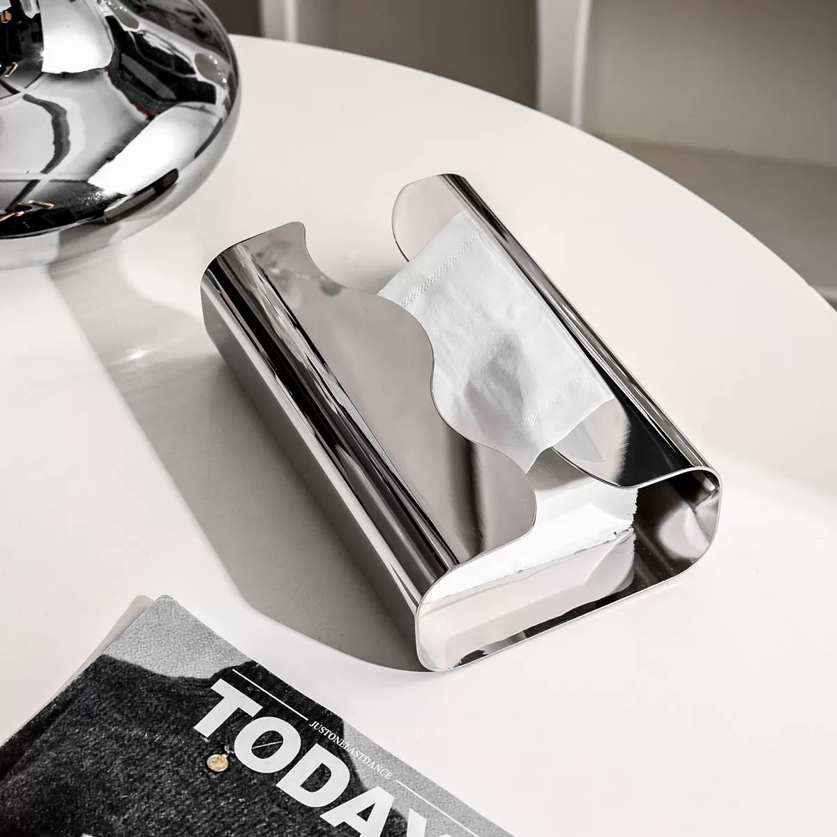 Chrome paper towel holder on a white surface with a magazine underneath