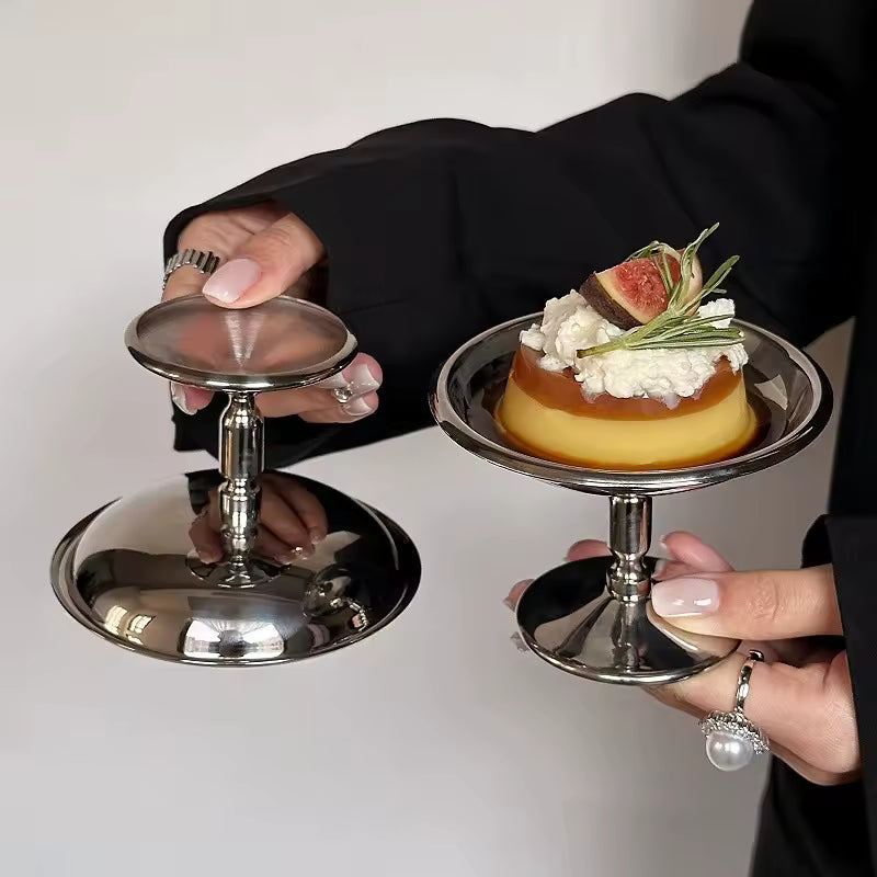 Person holding two small dessert stands with pastries on a plain background