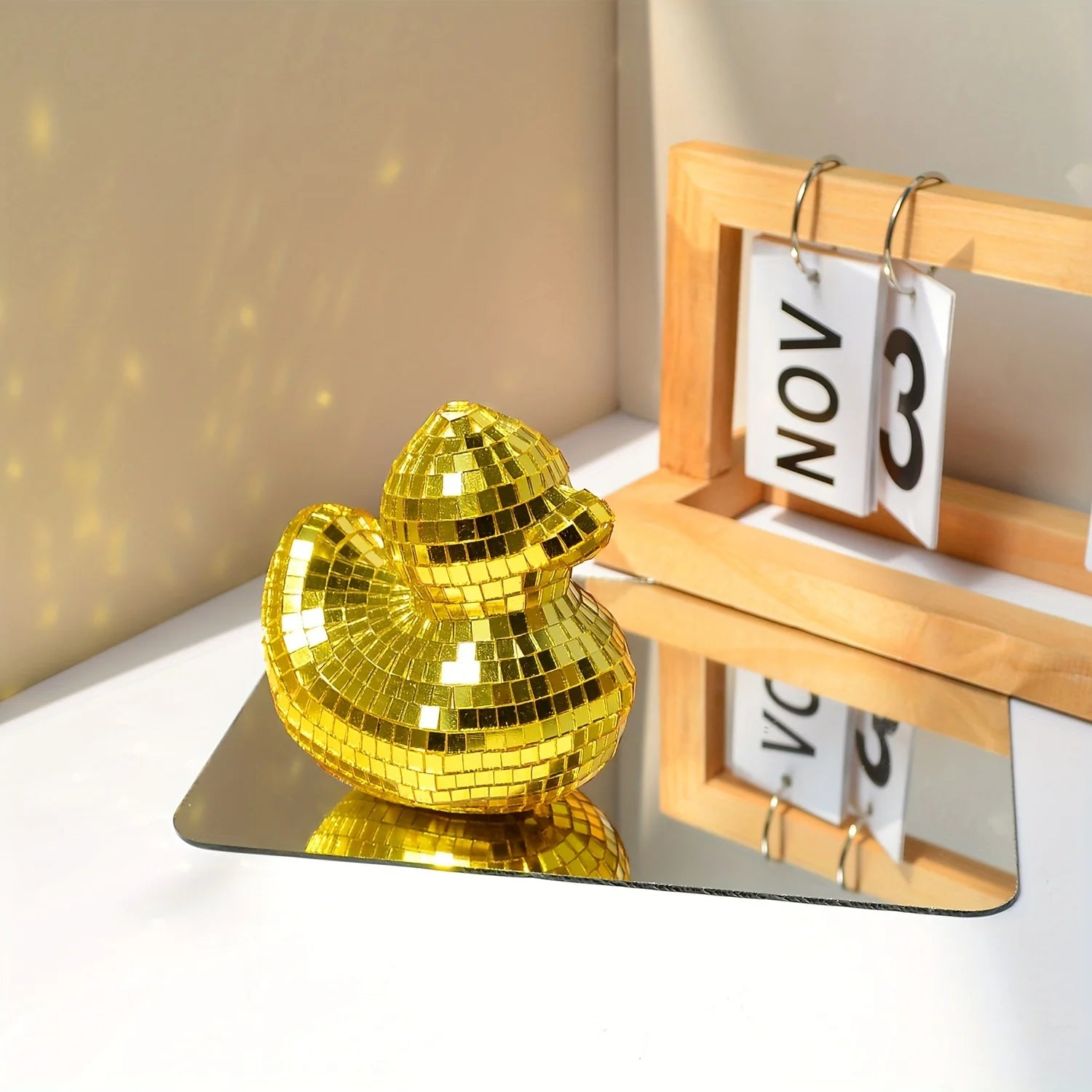 Gold disco duck on a reflective surface with a calendar in the background