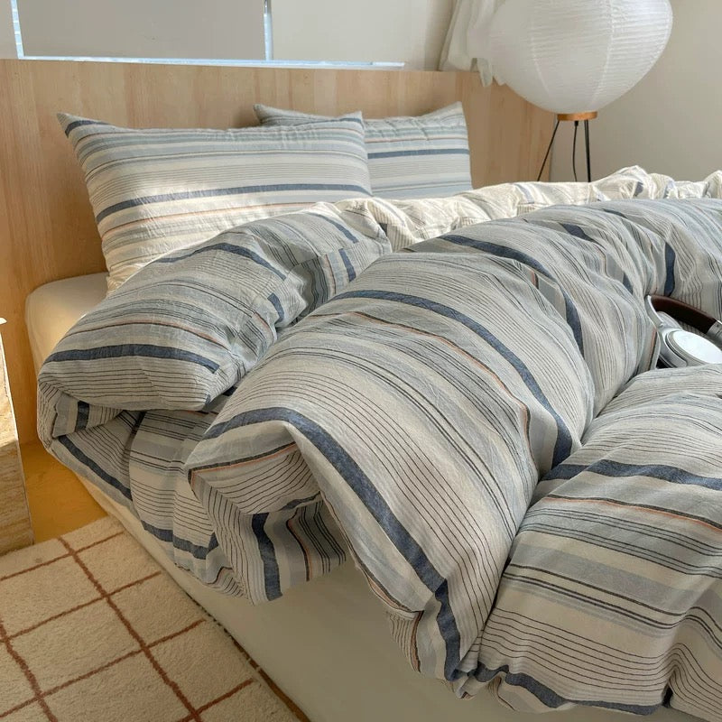 Striped bedding on a bed in a room with a lamp and window.