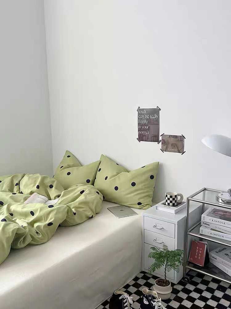 Bedroom with green polka dot bedding and a nightstand with decorative items.