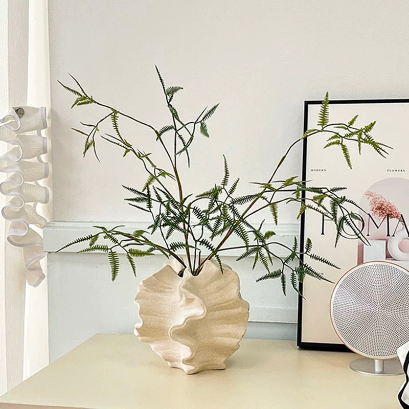 Decorative shell-shaped vase with green branches on a shelf