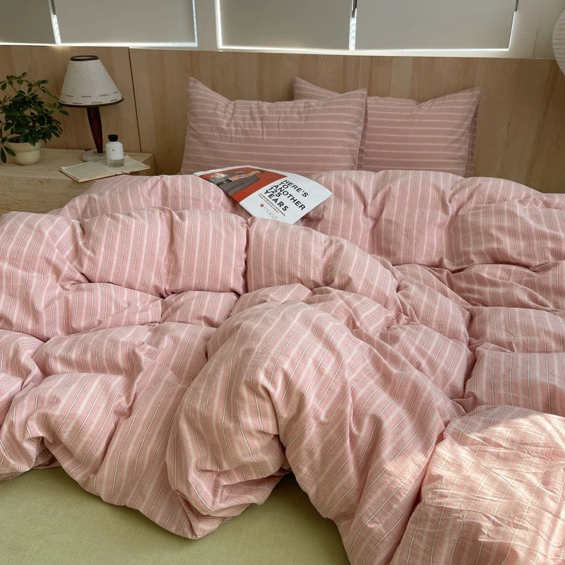 Pink striped bedding on a bed with a lamp and plant in the background.