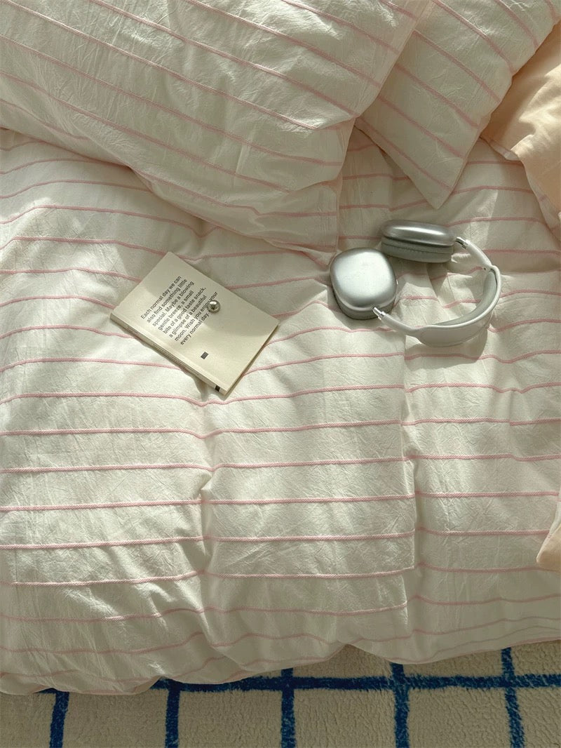 White comforter with red stripes on a bed, featuring a tag and a small round object.