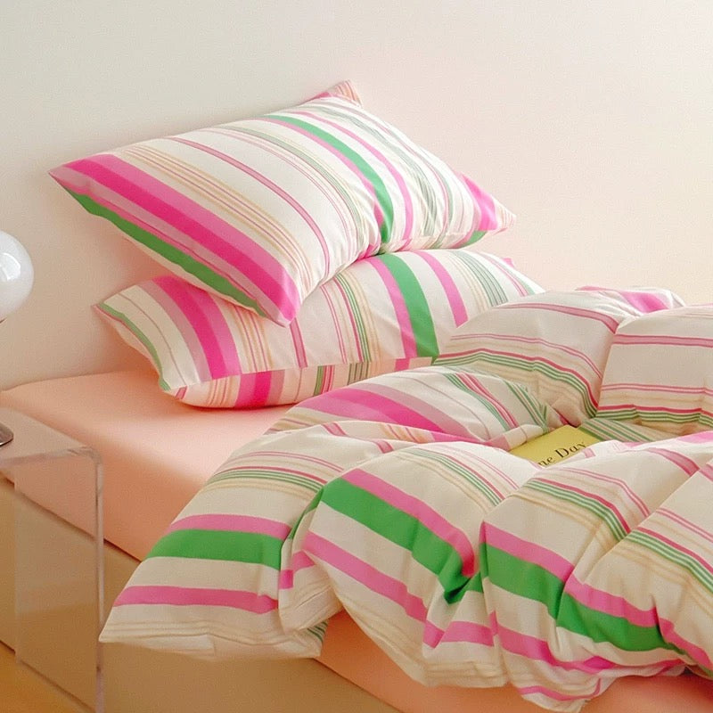 Striped pink and green bedding on a bed with a clear nightstand.