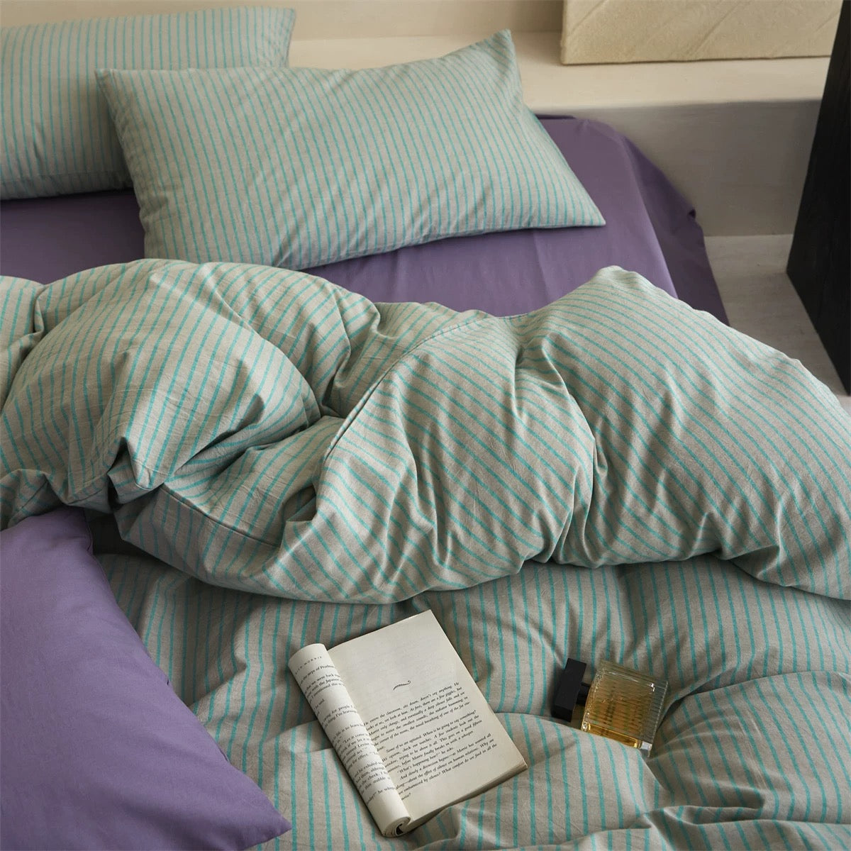 Bed with green and white striped bedding and purple pillows