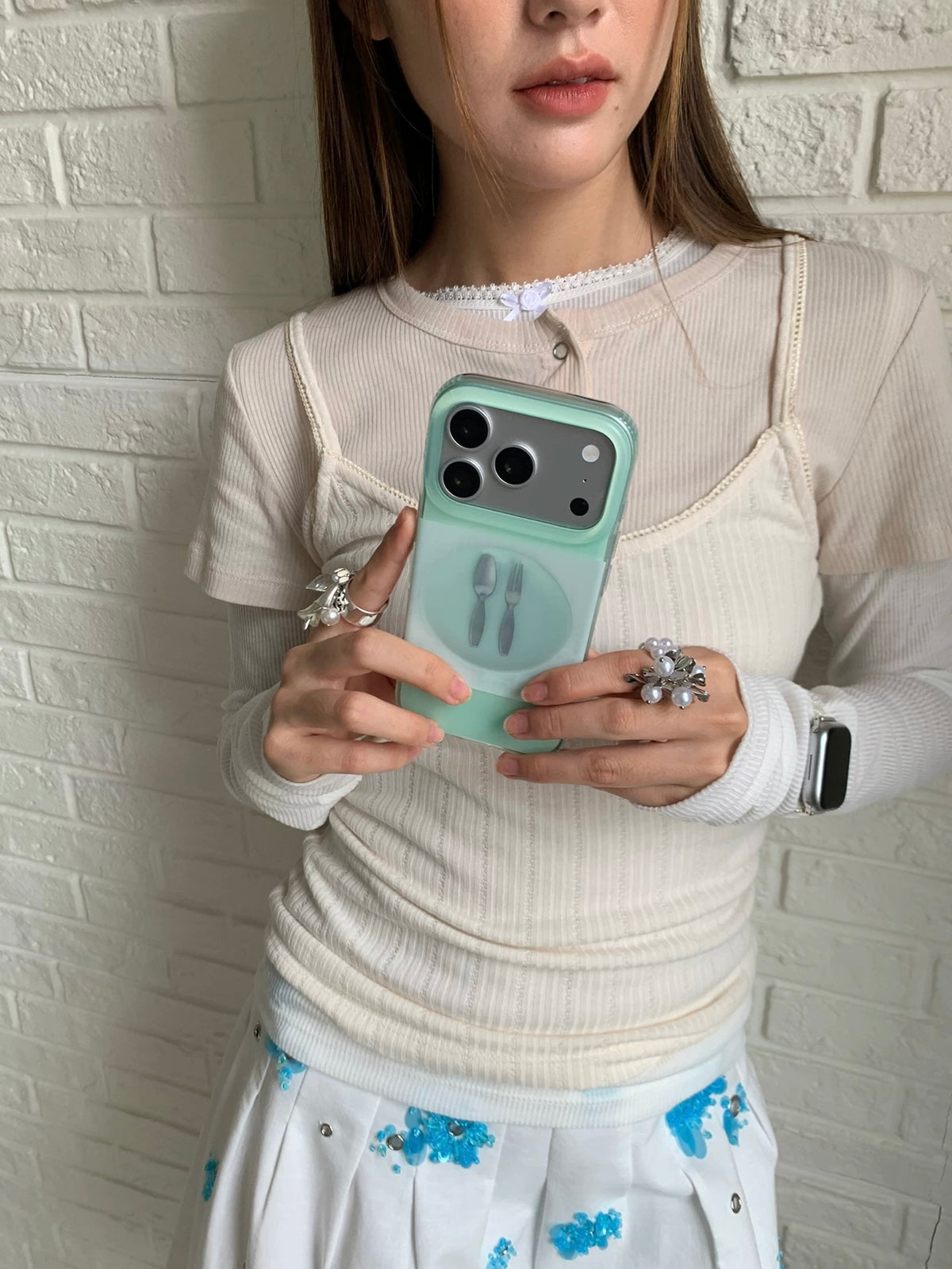 A mint fork phone case held upright near the chest, with a spoon and plate also visible on the back.