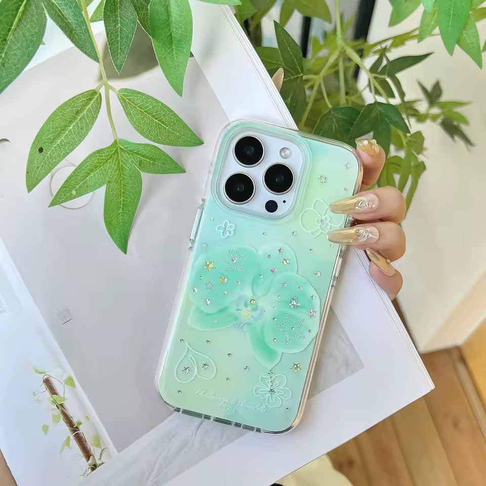 Phone case with floral design held by a hand, plant in the background