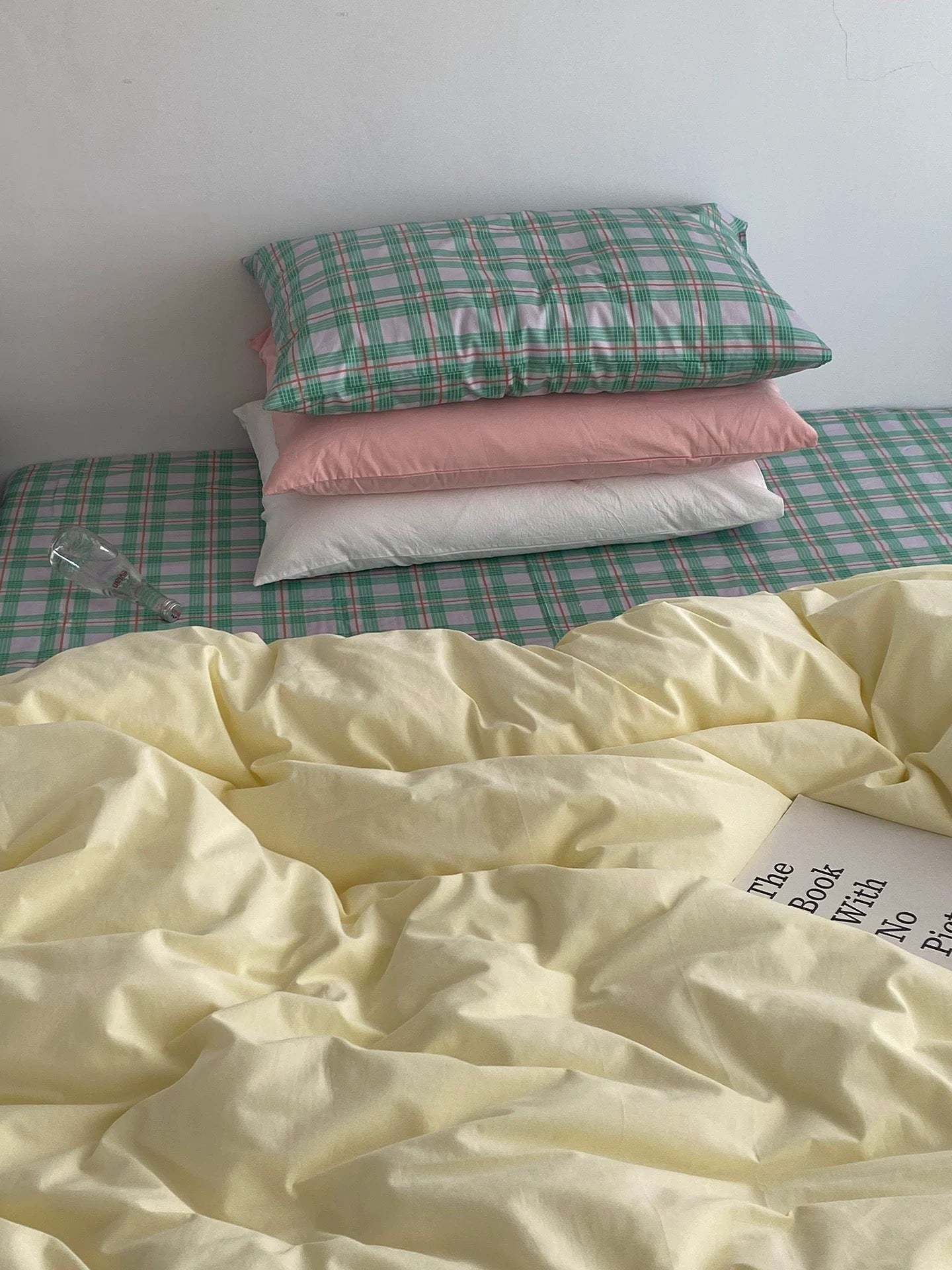 Stack of pillows and a blanket on a bed with a green checkered pattern.