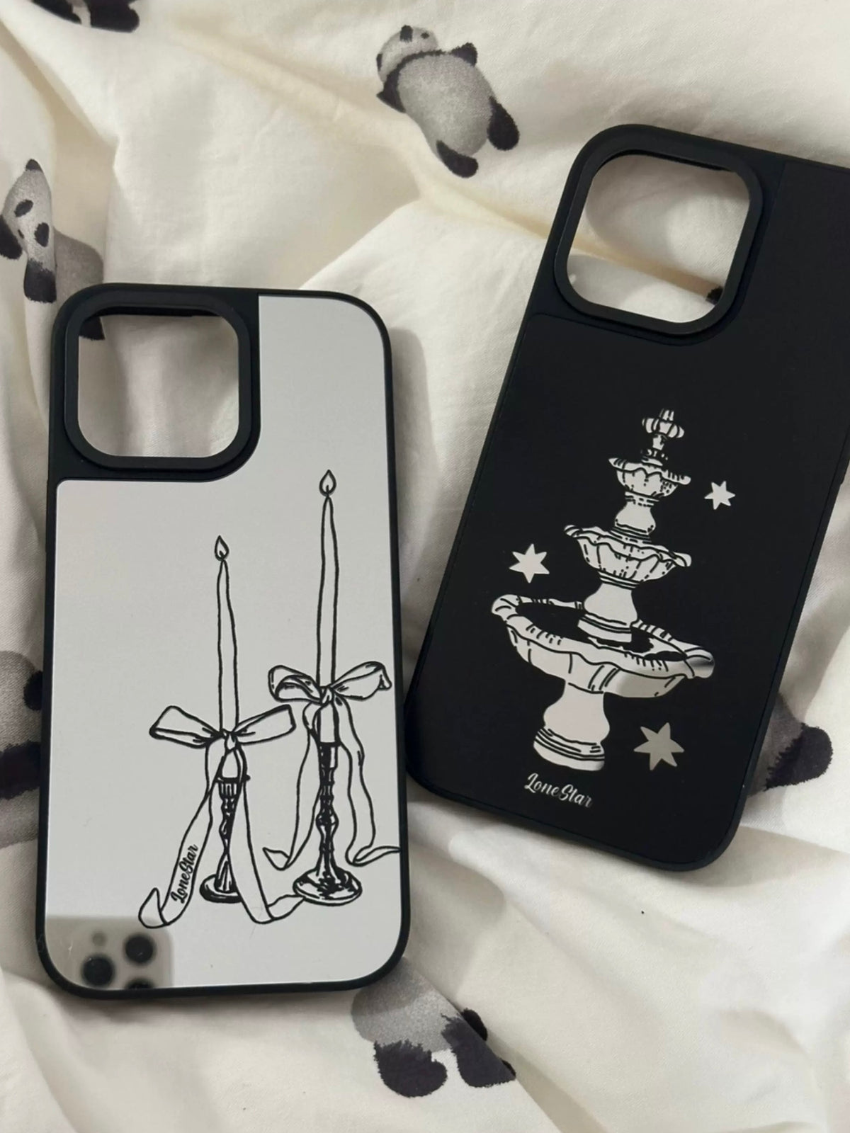 A mirror phone case pair shown upright, with bow candles on silver beside a fountain print on black.