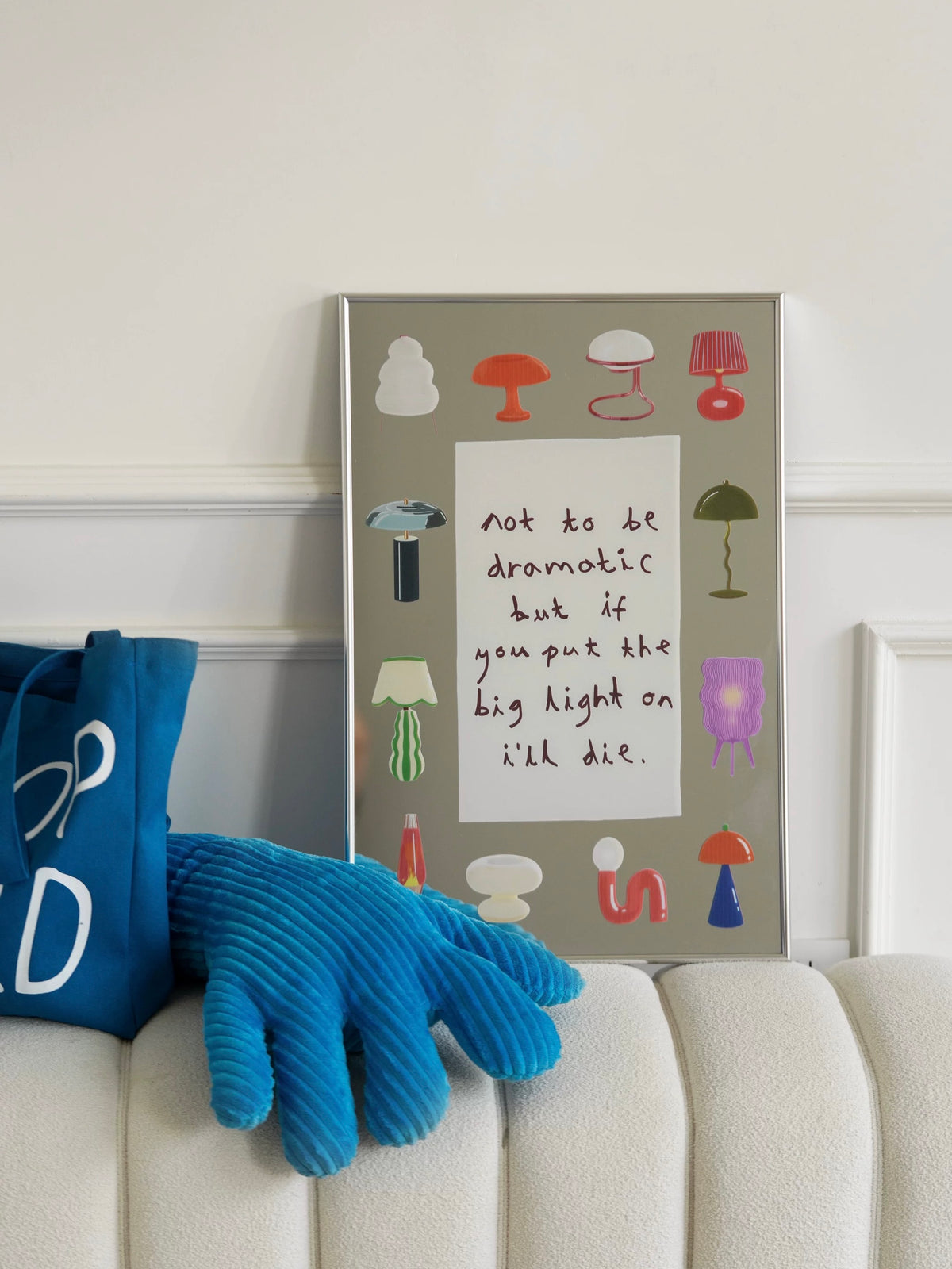 Mirror wall art with colorful lamp illustrations and handwritten text in a slim silver frame beside a sofa.