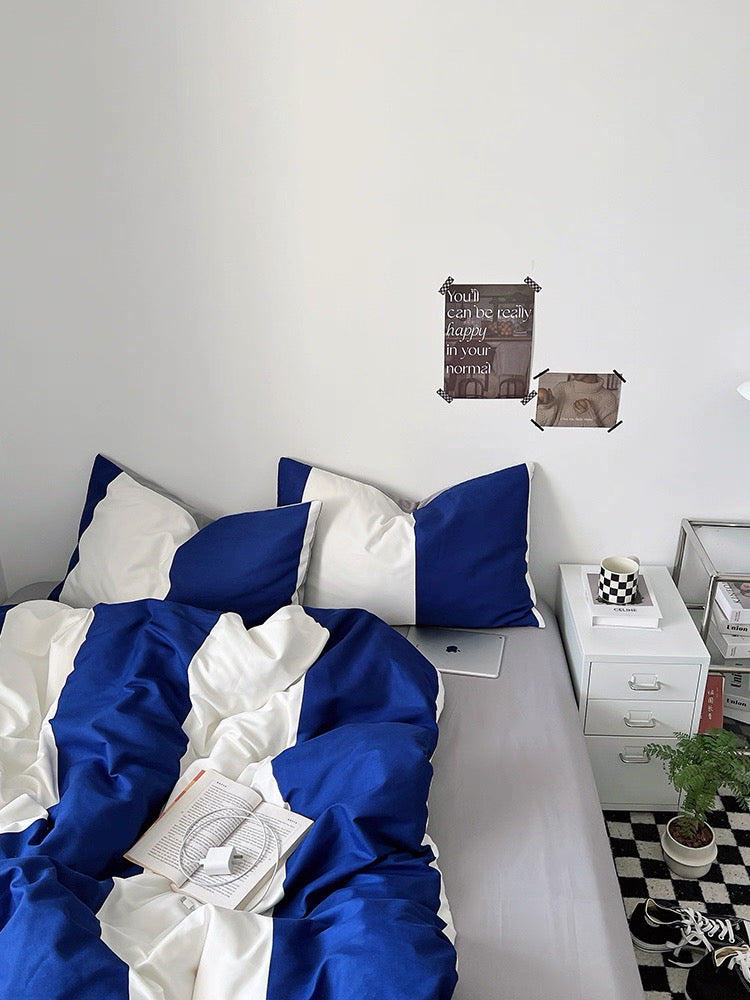 Bed with blue and white bedding in a room with a nightstand and decorative items.