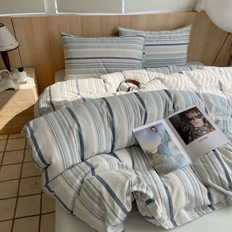 Bed with striped bedding and a magazine on a wooden floor.