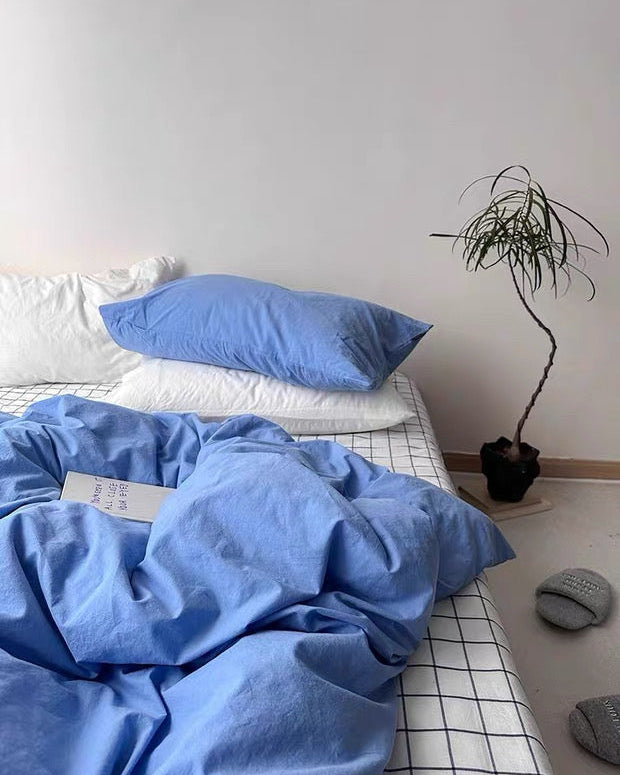 Blue bedding on a bed with white pillows and a plant in the corner.