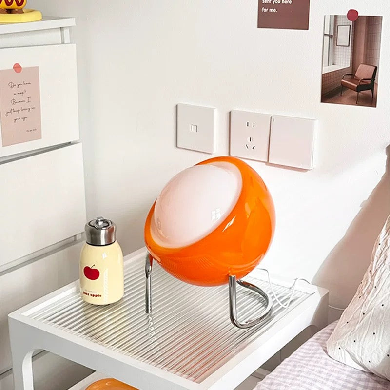Orange spherical lamp on a white side table with a water bottle featuring an apple design.