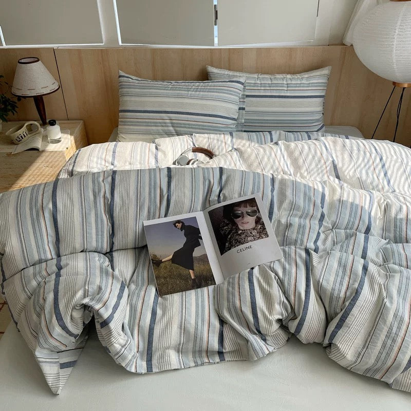 Bed with striped bedding and a magazine on top, in a room setting.