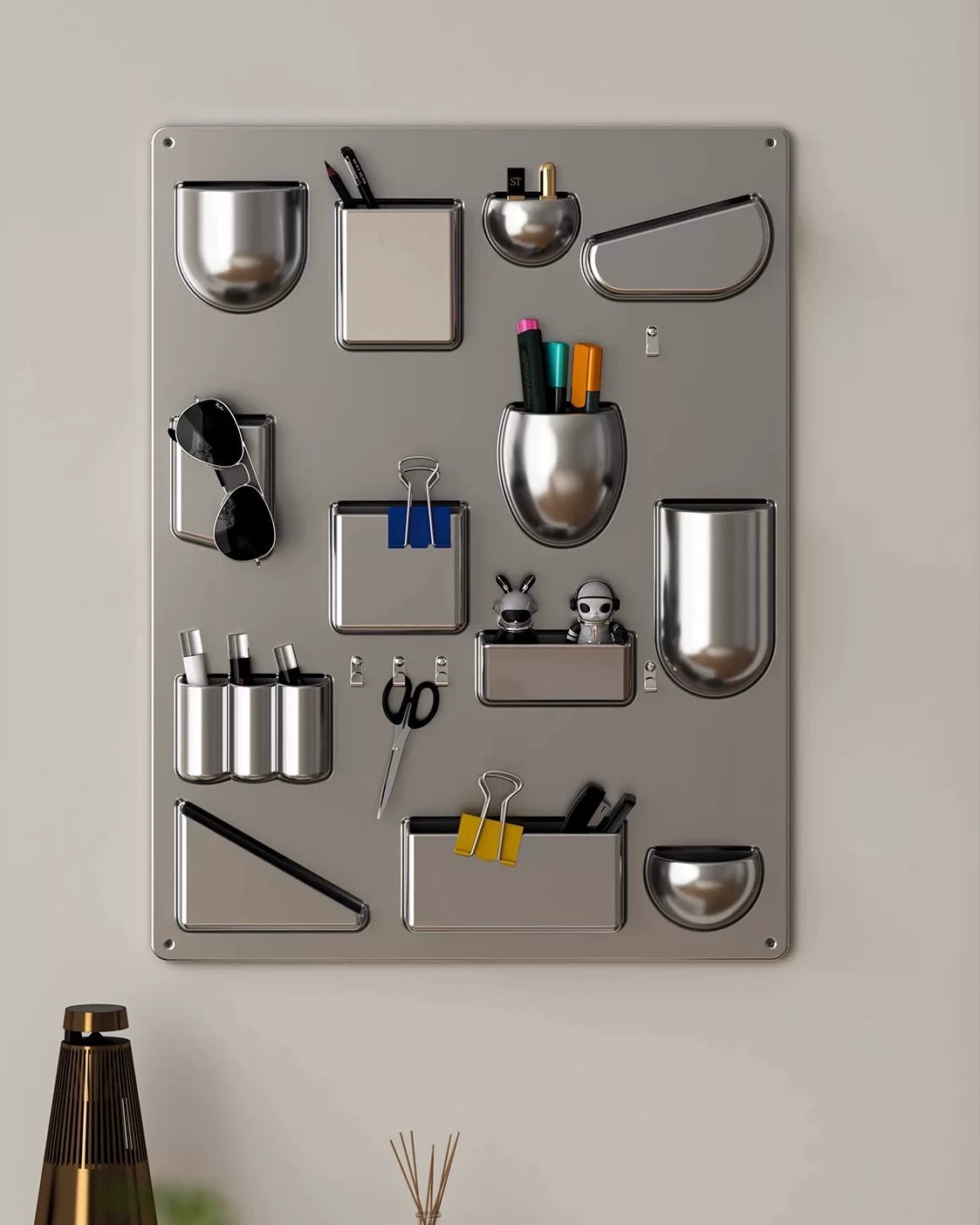 Metal wall organizer with various compartments and office supplies on a light gray background