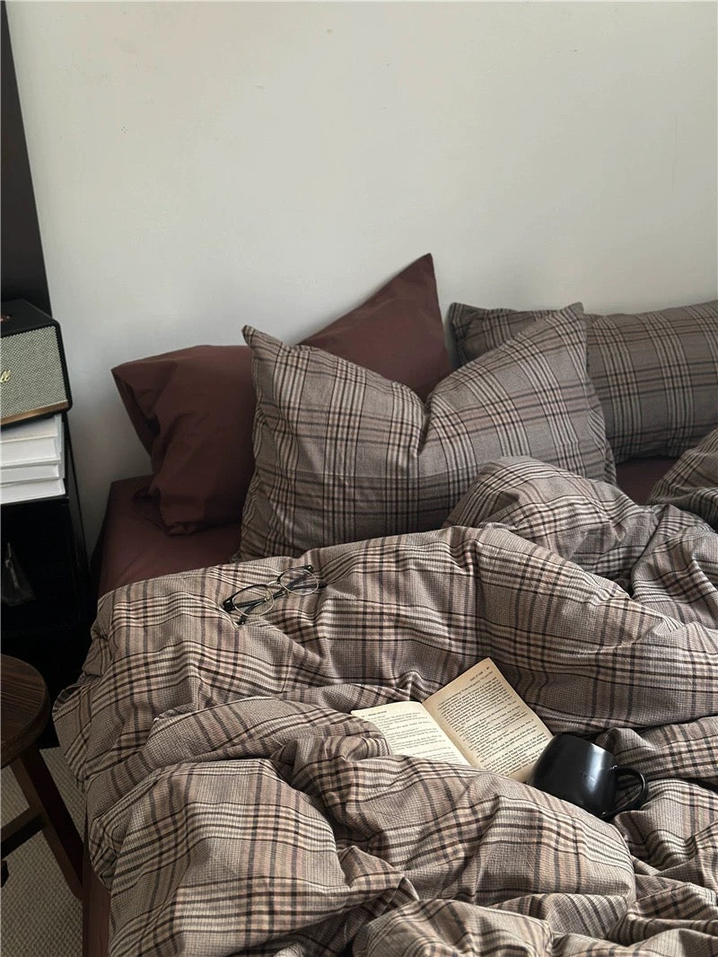 Plaid blanket and pillows on a sofa with a book underneath, in a cozy living room setting.
