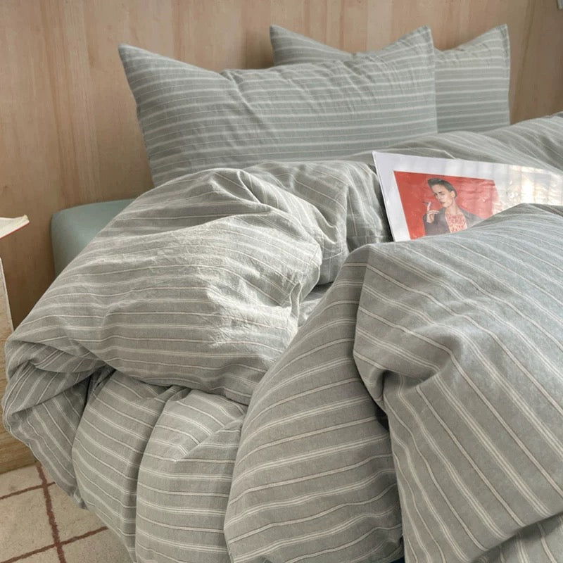 Bed with striped bedding and pillows, featuring a magazine and a small dog on a wooden floor.