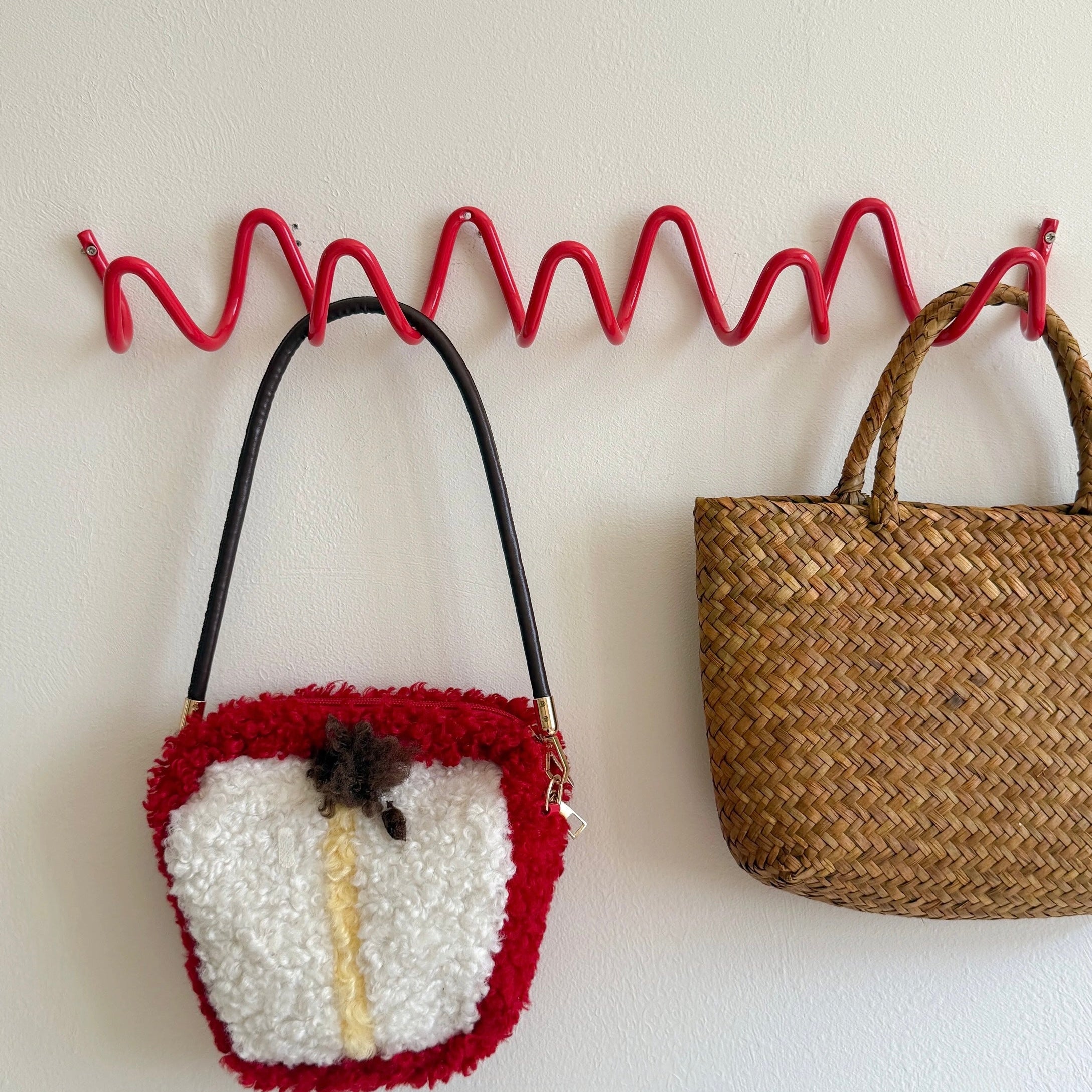 Two bags hanging on a red metal hook against a white wall.