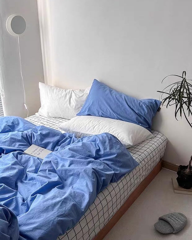 Blue bedding set on a bed with white pillows and a plant in the corner.