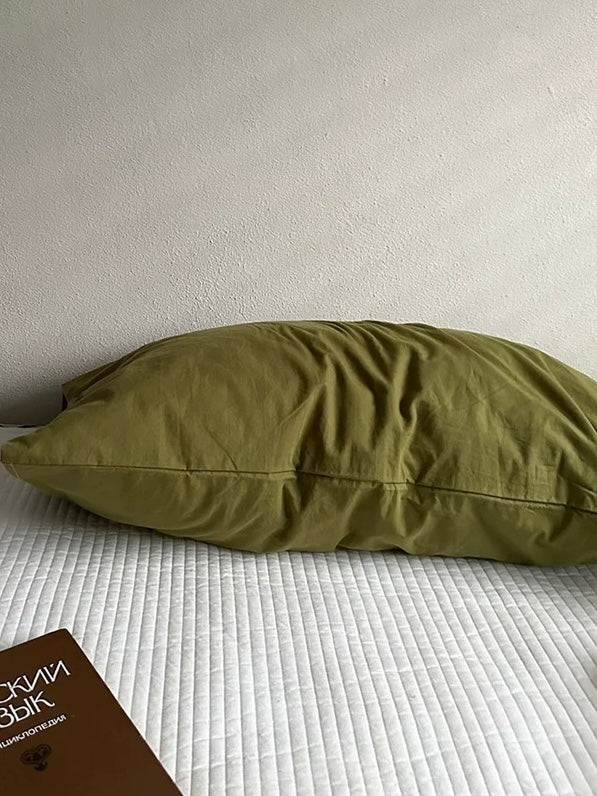 A solid olive green pillowcase on a white quilted bed.