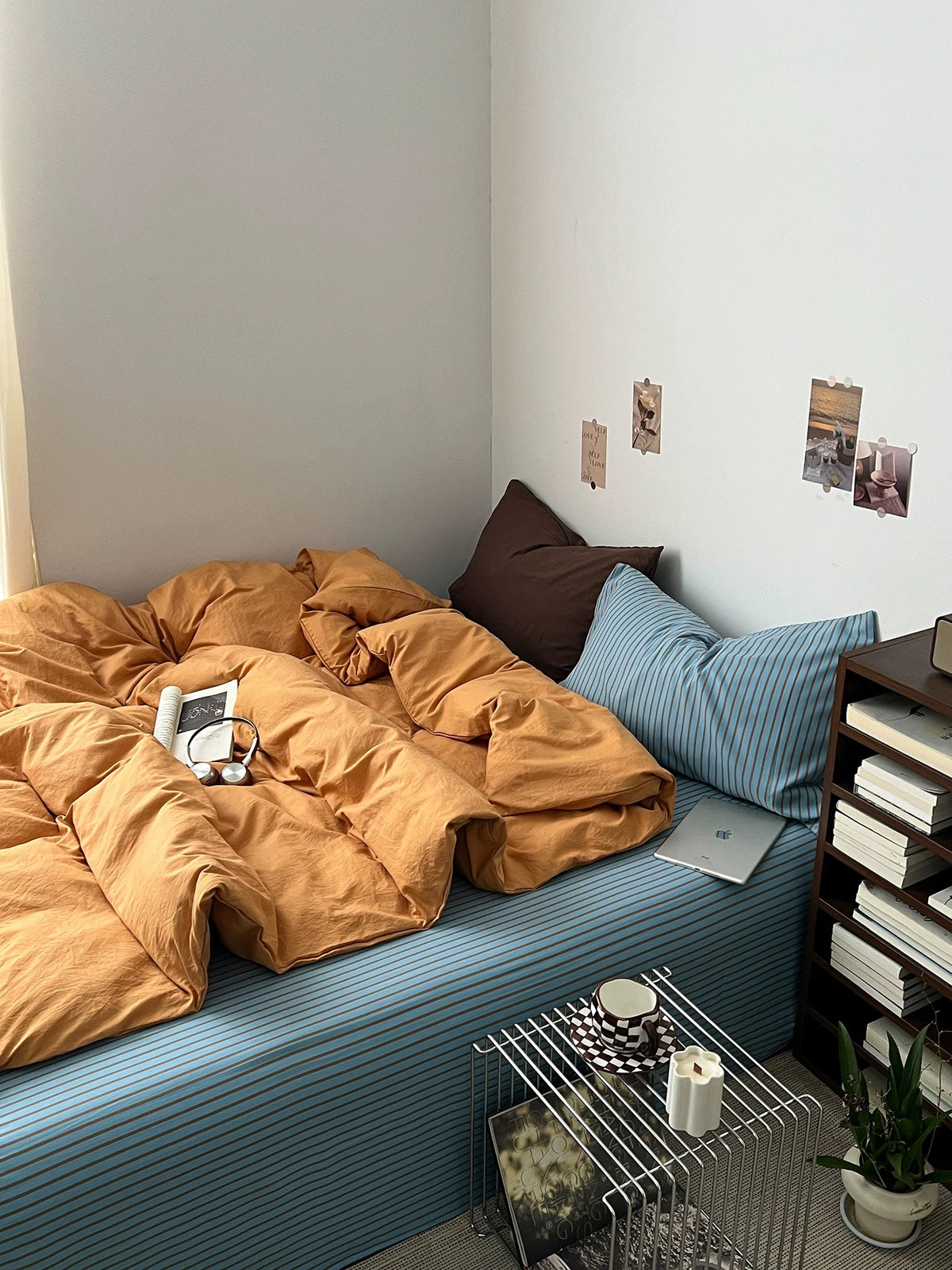 Side view of an orange duvet cover on a blue striped sheet beside a dark wood shelf