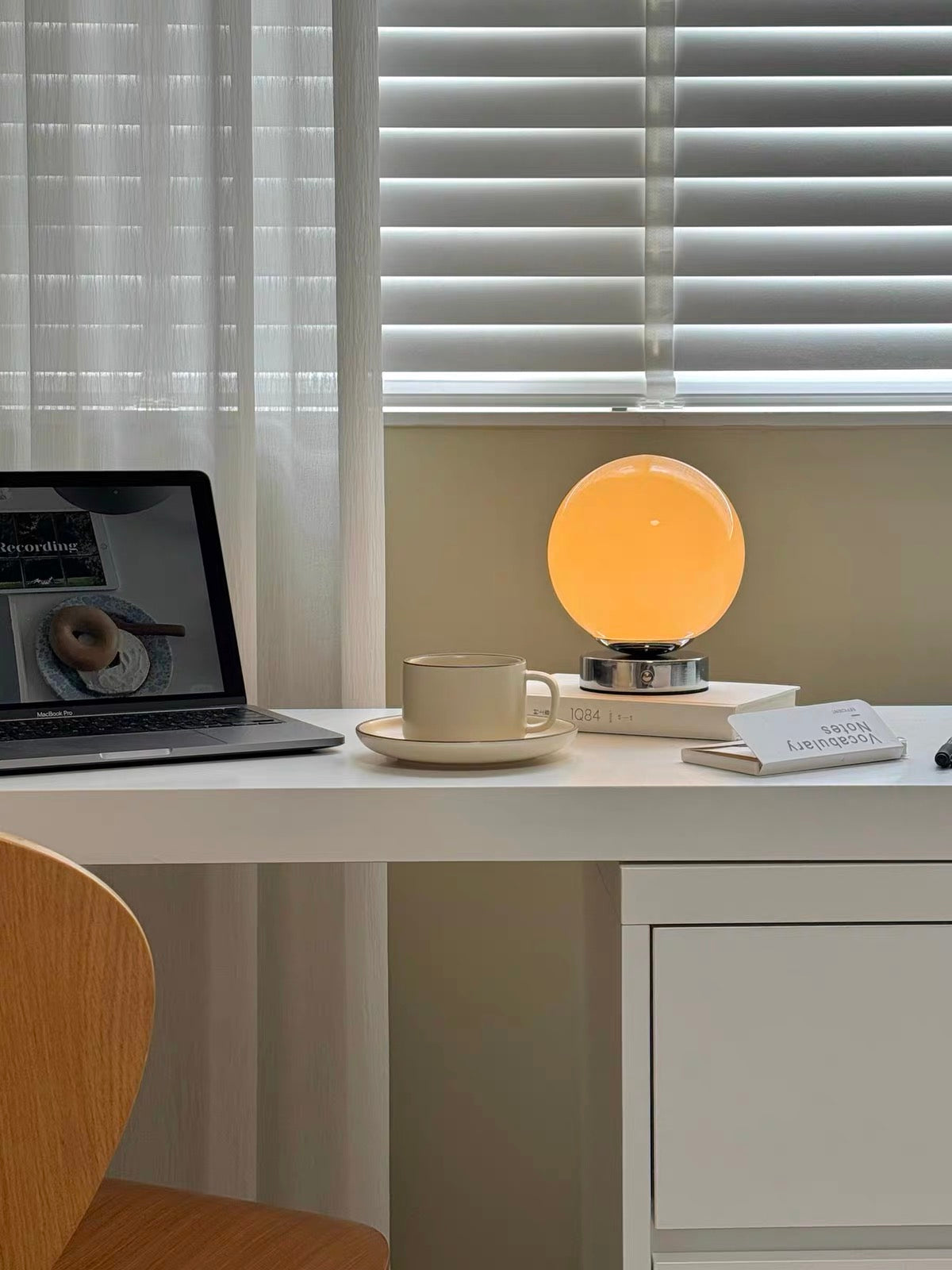 Desk with a laptop, mug, and round lamp under window blinds