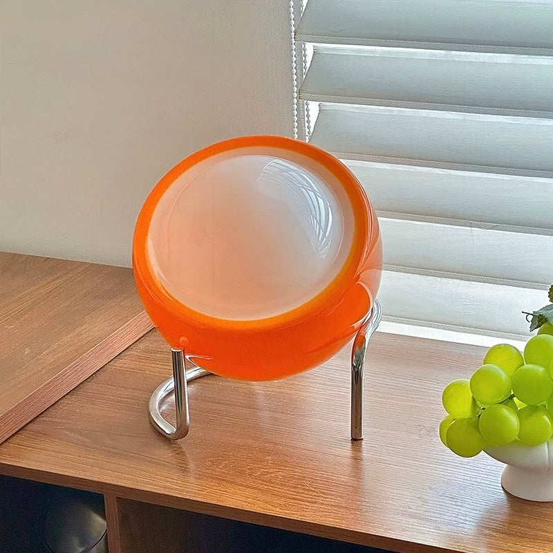 Orange and white spherical chair on a wooden table with grapes in the background