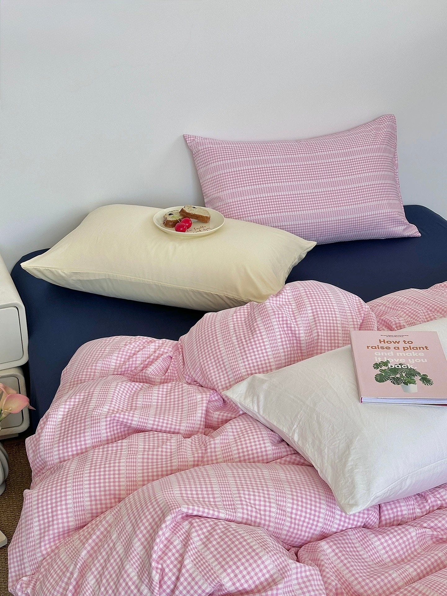Bed with pink checkered duvet and pillows against a white wall