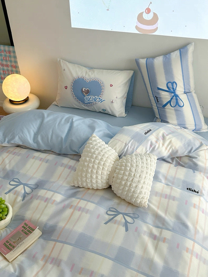 Bed with light blue bedding and decorative pillows, nightstand with lamp, and small plant.